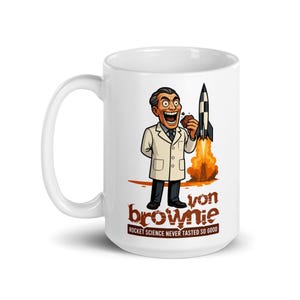 Könnte beinhalten: Weiße Keramiktasse mit einer Cartoon-Illustration eines Mannes im Laborkittel, der einen Brownie hält, mit einer Rakete im Hintergrund. Der Text lautet "von brownie" und "Rocket Science Never Tasted So Good."