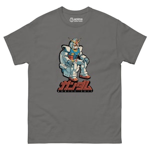 Può includere: T-shirt grigia con un robot dei cartoni animati seduto su un water. Il robot è bianco, blu, rosso e giallo. Il testo giapponese "GUNDAM" e il testo inglese "MOBILE SHIT" sono sotto.