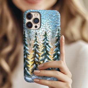 May include: A smartphone case featuring a winter forest scene. The design includes snow-covered evergreen trees with a golden sunset backdrop, set against a cracked ice-like blue background. The case has a glossy finish.