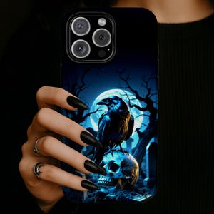 May include: Black phone case featuring a raven perched on a skull, set against a backdrop of a full moon, bare trees, and a graveyard. The design is predominantly blue and black, creating a gothic or Halloween theme.