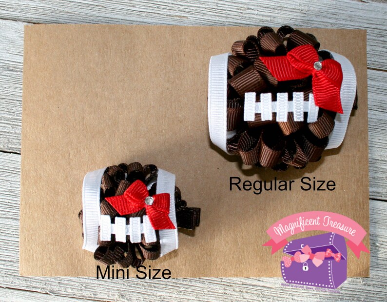 Puede incluir: Dos lazos para el pelo de color marr&oacute;n y blanco con tem&aacute;tica de f&uacute;tbol americano, con lazos rojos y pedrer&iacute;a. El lazo m&aacute;s peque&ntilde;o est&aacute; etiquetado como "Mini Size" y el lazo m&aacute;s grande est&aacute; etiquetado como "Regular Size".