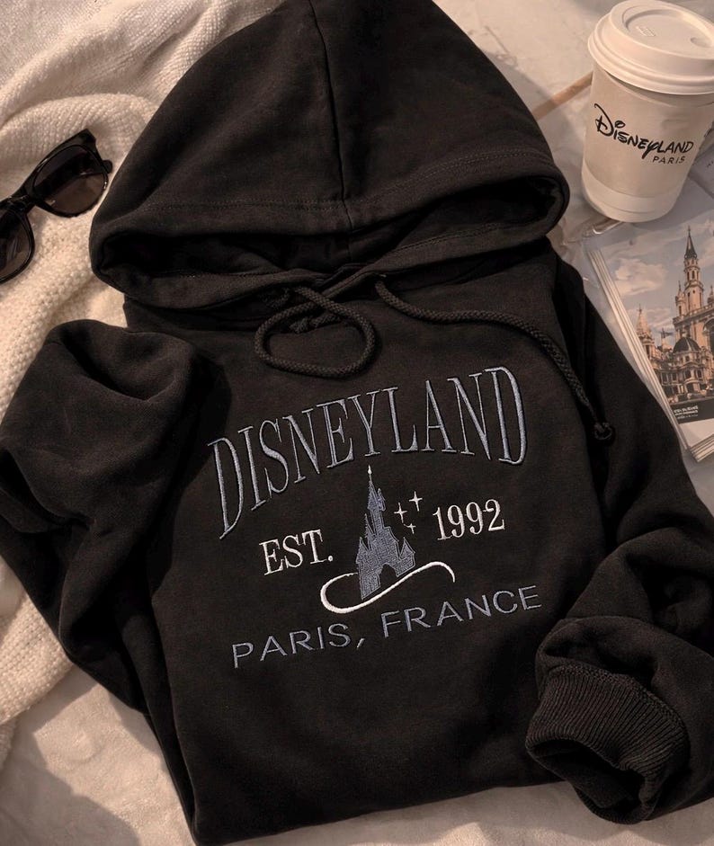 May include: A white ceramic mug with a black handle and the text "But First, Coffee" in a black, handwritten-style font. The mug is on a white surface.