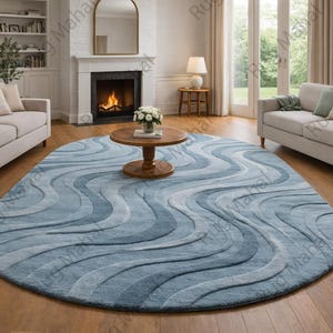 May include: An oval rug with a wave design in shades of blue and grey. The rug is the centrepiece of a living room with light-coloured sofas, a fireplace, and wooden flooring. The rug's design adds a touch of modern elegance to the room.