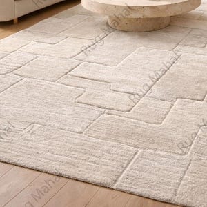 Ivory textured geometric area rug styled in a modern minimalist living room with neutral furniture.