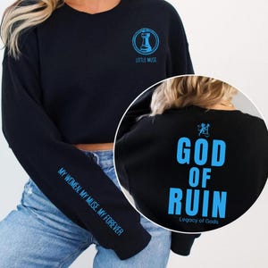 May include: Black sweatshirt with blue text and graphics. The front features a chess piece graphic and the words "LITTLE MUSE". The sleeve reads "MY WOMEN. MY MUSE. MY FOREVER". The back displays "GOD OF RUIN" and "Legacy of Gods".