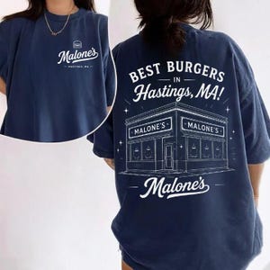 May include: Navy blue t-shirt with white text and graphics. The front features "Malone's" with a burger icon and "Hastings, MA." The back displays "BEST BURGERS in Hastings, MA!" with a detailed illustration of a restaurant.