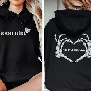 May include: Black hoodie with the words "GOOD GIRL" and a heart graphic on the front. The back of the hoodie features a heart made of skeleton hands with the text "STFUATTDLAGG".