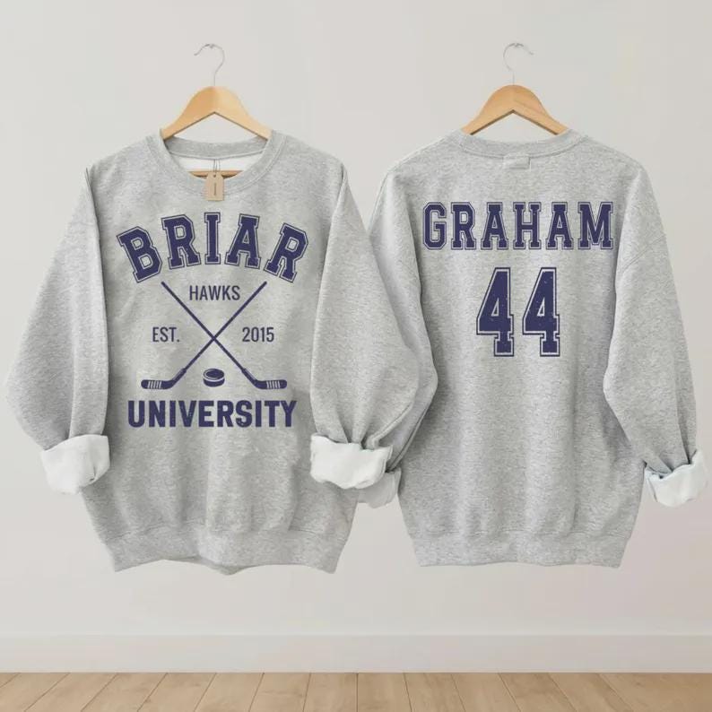May include: A heather gray sweatshirt with the text "BRIAR UNIVERSITY HAWKS" in navy blue, along with crossed hockey sticks and the year "2015". The back of the sweatshirt displays the name "GRAHAM" and the number "44" in navy blue.