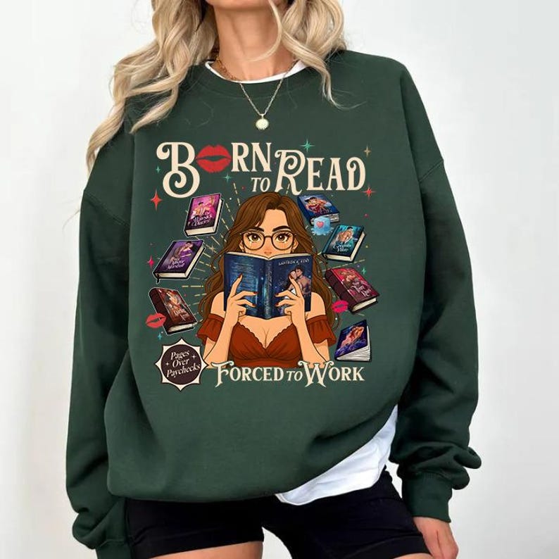 May include: Dark green sweatshirt with the text "Born to Read Forced to Work." The graphic features a woman reading surrounded by books. The design includes red lips, stars, and the phrase "Pages Over Paychecks."
