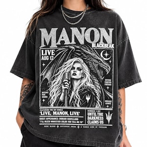 Könnte beinhalten: Ein anthrazitfarbenes Kurzarm-T-Shirt mit einem Grafikdruck einer Frau mit langem Haar, die ein Mikrofon vor einem Drachen hält. Der Text enthält "MANON BLACKBEAK," "LIVE AUG 12," "WITCHES RIDE HIGHER," "SISTERS FOREVER FURTHER," und "ABRAXOS ALWAYS."