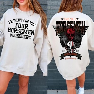 May include: A cream-coloured sweatshirt featuring black and red graphic text and skull designs. The front reads "PROPERTY OF THE FOUR HORSEMEN THUNDER BAY." The back features "THE FOUR HORSEMEN" and "DEVIL NIGHT" with skull illustrations.