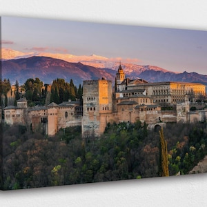 Puede incluir: Impresión en lienzo del palacio de la Alhambra en Granada, España, al atardecer. La imagen muestra la histórica fortaleza con sus torres y edificios, sobre un fondo de montañas nevadas y un cielo colorido.
