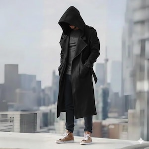 Könnte beinhalten: Ein langer schwarzer Mantel mit Kapuze und Gürtel, getragen über einem grauen Hemd und dunklen Jeans. Der Mantel hat ein klassisches Trenchcoat-Design mit Kapuze. Die Person trägt braune High-Top-Sneaker. Der Hintergrund ist eine verschwommene Stadtlandschaft.