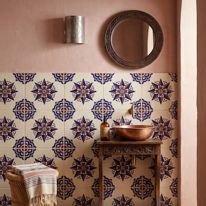 May include: A bathroom vanity area featuring a copper basin on a wooden table, a round mirror, and a wall sconce. The wall is covered in cream-colored tiles with a repeating blue and brown star pattern, set against a dusty pink wall.