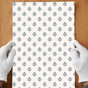 May include: A rectangular sheet of paper featuring a repeating pattern of small, blue-grey thistle illustrations arranged in a grid on a solid off-white background. The design consists of stylized floral motifs with stems and leaves.