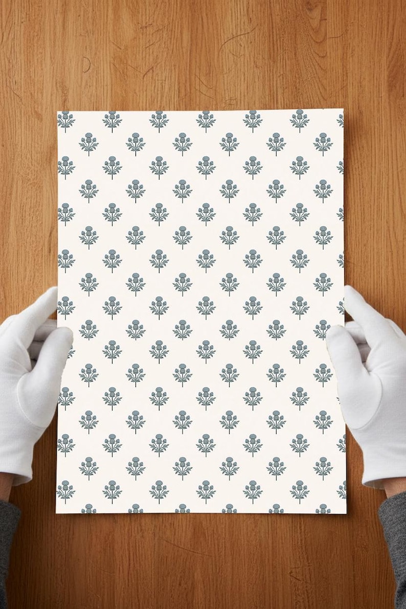 May include: A rectangular sheet of paper featuring a repeating pattern of small, blue-grey thistle illustrations arranged in a grid on a solid off-white background. The design consists of stylized floral motifs with stems and leaves.