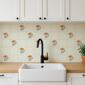 May include: A kitchen backsplash featuring square off-white tiles decorated with a repeating pattern of orange poppy flowers and green leaves, positioned above a wooden countertop with a white farmhouse sink and a matte black faucet.