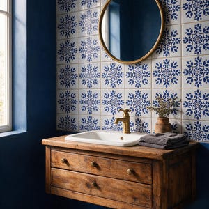 May include: A wall-mounted wooden vanity with two drawers and brass knobs, featuring a white rectangular sink and a brass faucet. Above, a round mirror with a gold frame hangs against a wall of white tiles with blue floral patterns.