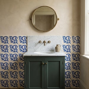 May include: A dark green vanity cabinet with a white marble countertop and backsplash, featuring a brass faucet and two handles. Above the vanity is a round brass-framed mirror. The wall is decorated with square tiles featuring blue scrollwork.