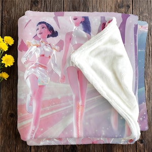 May include: A pink and white blanket featuring a digital illustration of two women in futuristic outfits. The blanket has a soft, plush texture with a white underside. The design includes a light pink and purple background.