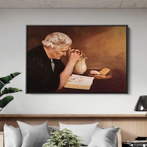 Op de afbeelding: Een ingelijst schilderij toont een oudere persoon met wit haar, gekleed in het zwart, met de handen gevouwen in gebed over een open boek. Een witte kan en een stuk brood staan op tafel. De achtergrond is een warme sepia tint.