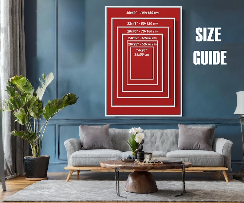 Puede incluir: Un cuadro rojo y blanco enmarcado con una gu&iacute;a de tallas, con medidas en cent&iacute;metros y pulgadas. El cuadro se muestra en una pared azul sobre un sof&aacute; gris. El texto "SIZE GUIDE" es blanco.