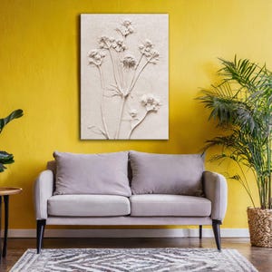 Puede incluir: Una obra de arte floral en relieve de tonos neutros cuelga sobre un sof&aacute; gris. La obra de arte presenta una representaci&oacute;n detallada de flores con tallos y hojas. La habitaci&oacute;n tiene una pared amarilla, una alfombra estampada y una planta en maceta.
