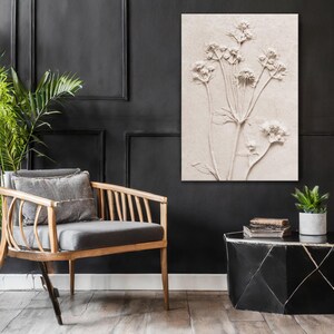 Puede incluir: Una obra de arte floral en relieve de tonos neutros cuelga de una pared negra. Una silla de madera con cojines grises y una peque&ntilde;a mesa auxiliar negra con una planta y libros completan la decoraci&oacute;n de la habitaci&oacute;n.