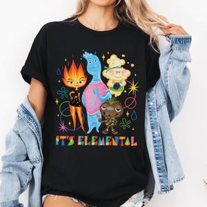 May include: Black t-shirt featuring a colorful graphic of animated characters from the movie "Elemental." The design includes a fire character, a water character, a cloud character, and a wood character, with the text "IT'S ELEMENTAL" in rainbow colors.