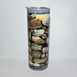 Könnte beinhalten: Ein hoher, zylindrischer Becher mit Deckel, der eine Collage aus bunten Steinen und den Text "Great Lakes Rocks" zeigt. Die Steine sind mit Namen wie "Leland Blue" und "Lake Superior Agate" auf schwarzem Hintergrund beschriftet.