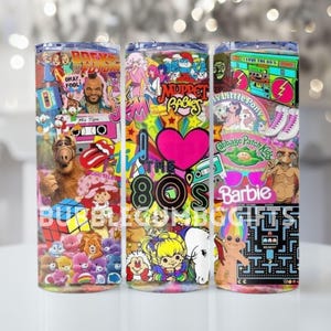 May include: Three stainless steel tumblers with a wrap-around design featuring 1980s pop culture icons. The design includes images of Alf, Mr. T, Barbie, and the text "The 80s". The tumblers are cylindrical and have a clear lid.