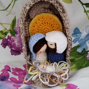 May include: Crocheted nativity scene with a brown, beige, and yellow manger, a blue and white Mary, a blue and white Joseph, and a white baby Jesus in a yellow and blue swaddle.