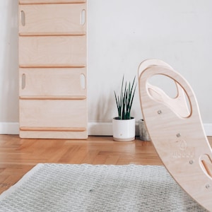 Può includere: L'immagine presenta un arco rampicante e una scala rampicante in legno. L'arco è curvo con un manico, e la scala ha diversi pioli. È visibile anche una piccola pianta in un vaso bianco.