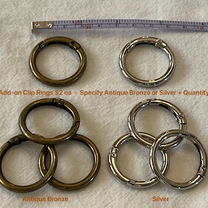 May include: An assortment of metal clip rings in antique bronze and silver. The image includes a measuring tape and text that reads "Add-on Clip Rings". The rings are shown in groups of one and three.