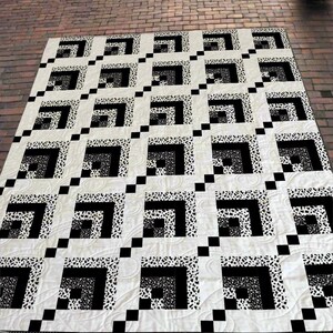 May include: A large, rectangular quilt with a repeating geometric pattern. The design features squares within squares in black and white, with some sections having a speckled pattern. The quilt is laid out on a brick surface.