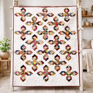 May include: A white quilt featuring a repeating pattern of colourful, cross-shaped designs. Each cross is made up of fabric patches in red, blue, green, and yellow. The quilt has a red border.