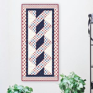 May include: A rectangular quilt with a patriotic theme, featuring a central design of interwoven blue and white sections. The quilt is bordered with a pattern of red stars on a white background, and the overall color scheme includes red, white, and blue.