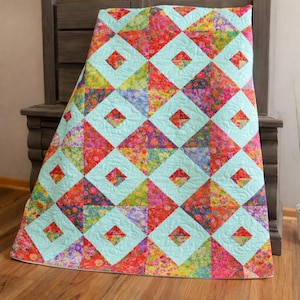 May include: A colorful quilt with a geometric pattern. The quilt features a repeating design of diamonds and squares in shades of red, pink, yellow, blue, and green. The squares are a light blue color, and the diamonds are a floral pattern.