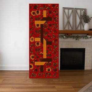 May include: A rectangular red rug with a floral pattern of sunflowers and berries. The rug features a geometric design in shades of brown and orange. The rug is placed on a wooden floor.