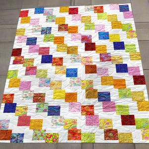 Könnte beinhalten: Ein farbenfroher Patchwork-Quilt mit weißem Hintergrund und zahlreichen Quadraten in verschiedenen Farben. Die Quadrate sind mit gemusterten Stoffen in Rot-, Blau-, Gelb-, Orange- und Grüntönen gefüllt. Der Quilt ist wahrscheinlich aus Baumwolle.