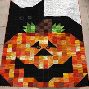 May include: A handmade Halloween quilt featuring a black cat and a jack-o'-lantern design. The quilt is made of squares in shades of orange, yellow, black, and white. The cat's eyes are represented by two black buttons.