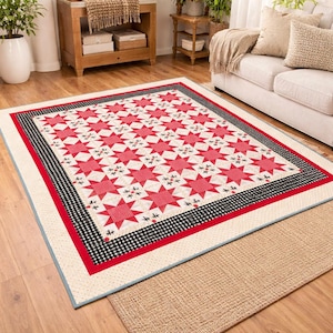 May include: A large, rectangular quilt with a star pattern in red and white. The quilt has a black and white checkered border, a red border, and a cream-colored edge. The quilt is placed on a wooden floor.