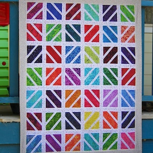 May include: A patchwork quilt with a repeating geometric design. Each square contains a diagonal stripe in a bright colour, such as red, blue, green, and purple, set against a white backdrop. The quilt is edged with a dotted fabric.