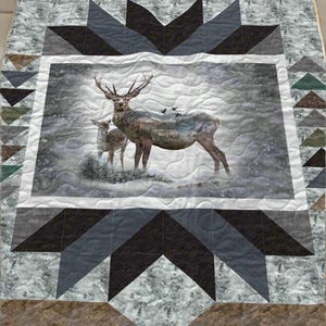 May include: A quilted blanket featuring a central image of two deer in a snowy landscape. The quilt has a starburst design in shades of gray, black, and brown, with a patterned border. The overall design evokes a rustic, nature-inspired theme.
