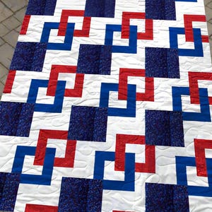 Könnte beinhalten: Eine handgefertigte Steppdecke mit einem geometrischen Muster in Rot, Weiß und Blau. Das Design zeigt ineinandergreifende Quadrate und Linien, die eine moderne und patriotische Ästhetik schaffen. Die Steppdecke ist wahrscheinlich aus Baumwollstoff.