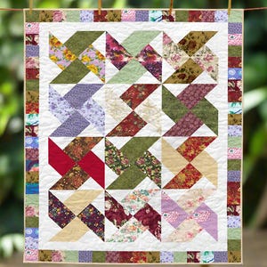 May include: A handmade quilt with a white background and a pattern of colorful pinwheels. The pinwheels are made from various floral fabrics in shades of red, green, purple, and yellow. The quilt is bordered with a patchwork design.