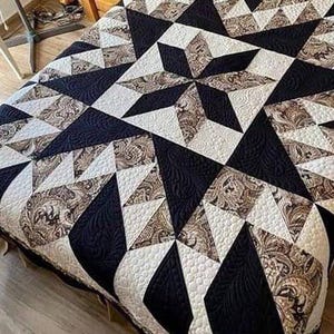 Peut inclure: Une courtepointe artisanale avec un motif géométrique en forme d'éclat d'étoile. La courtepointe présente des tissus noirs, blancs et bruns à motifs. La courtepointe est matelassée avec un motif de couture détaillé. La courtepointe est probablement de taille queen ou king.