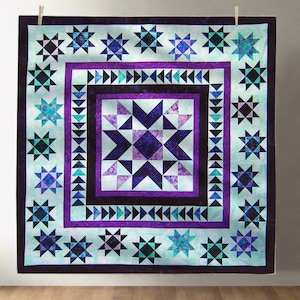 May include: A handmade quilt with a star pattern in shades of purple, blue, and teal. The quilt features a central star design surrounded by multiple star motifs and geometric borders. The quilt is displayed hanging from a clothesline.