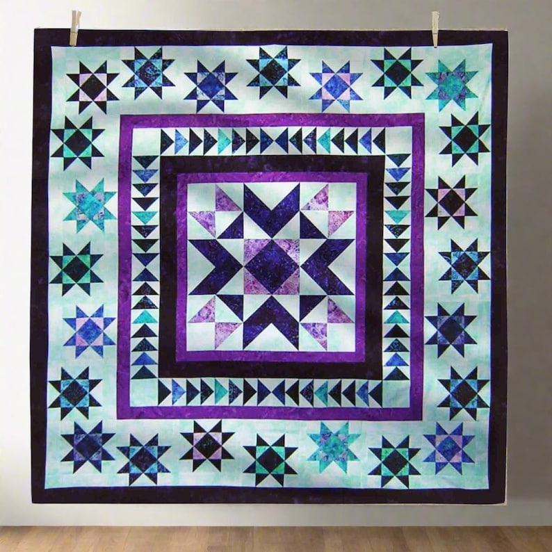 May include: A handmade quilt with a star pattern in shades of purple, blue, and teal. The quilt features a central star design surrounded by multiple star motifs and geometric borders. The quilt is displayed hanging from a clothesline.