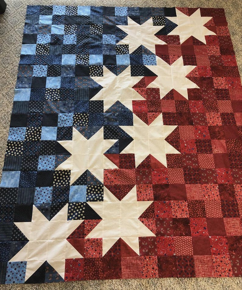 May include: A handmade quilt with a patriotic theme. The quilt features a design of alternating red and blue squares, with large white star shapes. The colours are arranged to create a flag-like pattern, ideal for home decor.